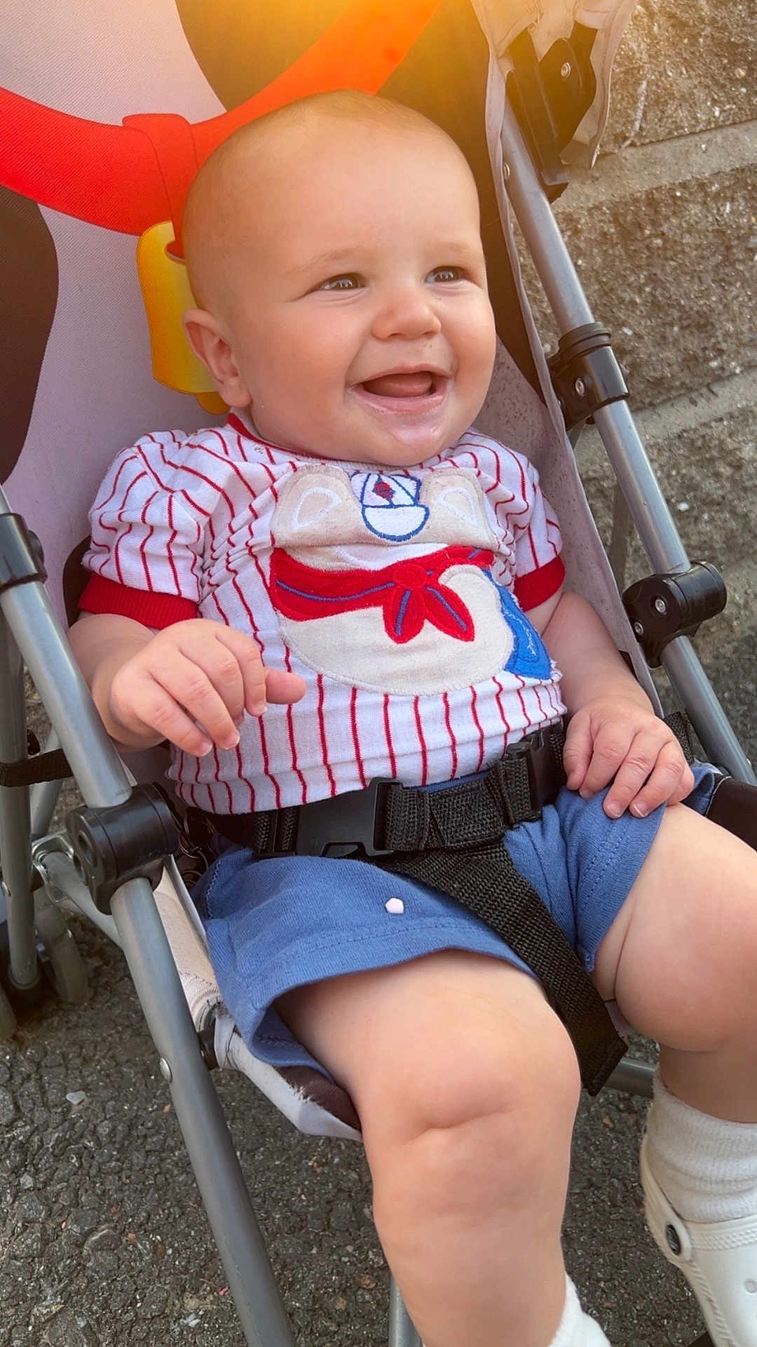Vincent joined the competition — help win amazing prizes! baby, smiling, stroller, outdoor, child, shorts, shirt, happy, sunlight, seatbelt, baby_clothing, footwear, white_shoes, concrete, metal_frame, playful, cute, infant, young_child, daylight