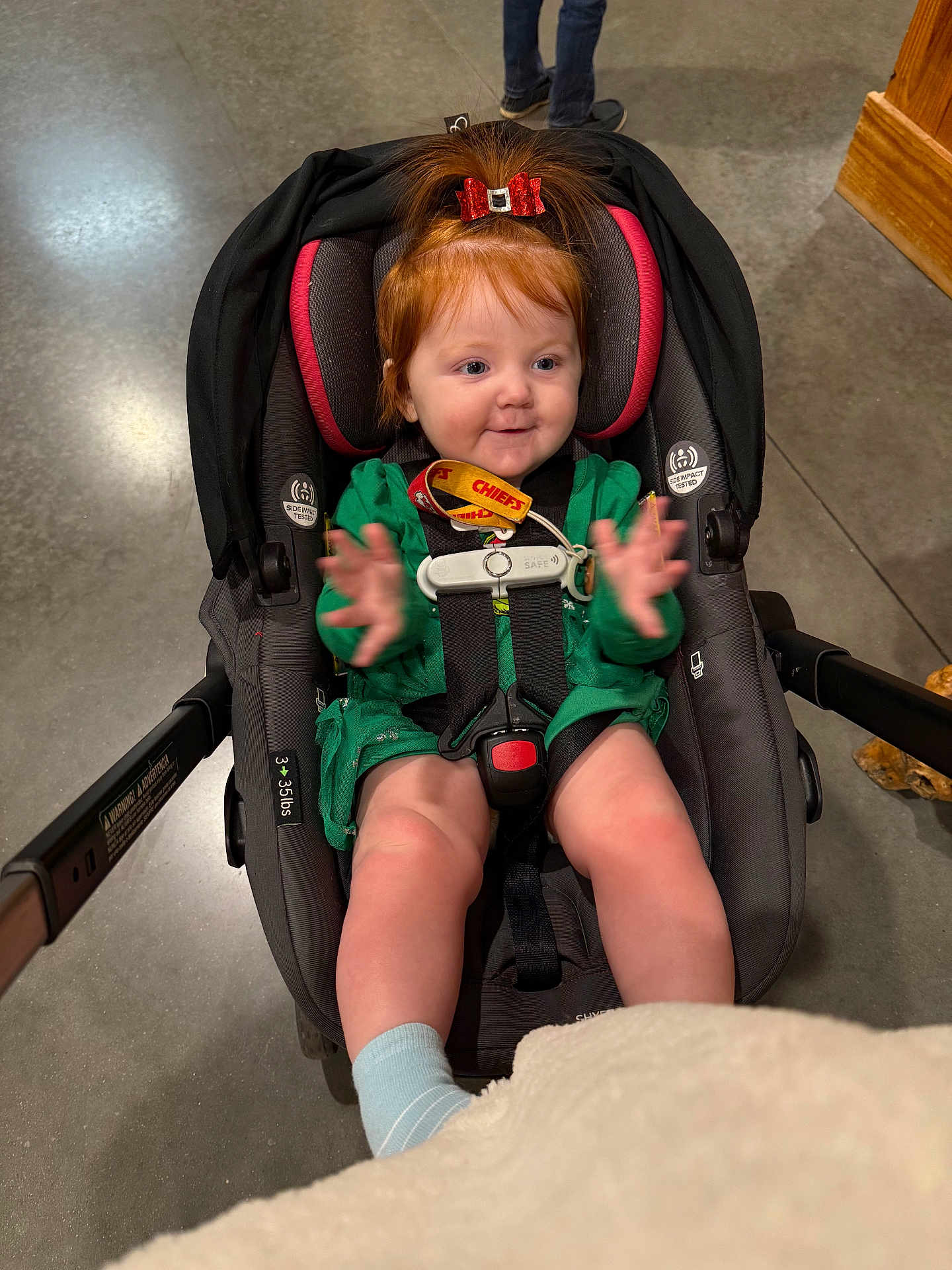 Evalyna is registered to the contest to win money with this photo: toddler, child, car_seat, clapping, red_bow, green_dress, baby, happy, indoor, floor, concrete, person, footwear, legs, strap, seatbelt, cute, expression, infant, smile