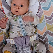 Kieran is registered to the contest to win money with this photo: baby, infant, pajamas, animal_print, seat, cushion, pattern, geometric, child, face, hands, clothing, indoor, comfort, cute, young, expression, portrait, resting, fabric