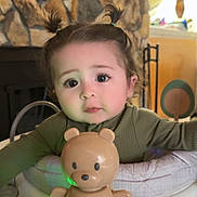 Willow is registered to the contest to win money with this photo: child, baby, toddler, face, big_eyes, pigtails, toy_bear, activity_center, jumper, indoor, lamp, stone_wall, fireplace, green_light, baby_seat, cute, curious_expression, hands, playtime, portrait