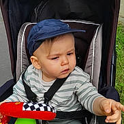 Adrien participe au concours pour gagner de l'argent avec cette photo : baby, cap, child, clothing, colorful, expression, grass, hand, headwear, outdoor, pavement, person, play, pointing, seatbelt, stroller, toddler, toy, transport, wheel