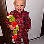 child, pajamas, plush_toy, grinch, red, blue, smile, indoor, carpet, door, wood, toy, footwear, cute, happy, person, clothing, standing, holiday, face