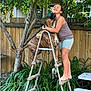 Leo is registered to the contest to win money with this photo: girl, dog, ladder, backyard, tree, plants, wooden_fence, greenery, barefoot, hugging, affection, smiling, outdoor, summer, pet, animal, playful, sunlight, casual_clothing, nature