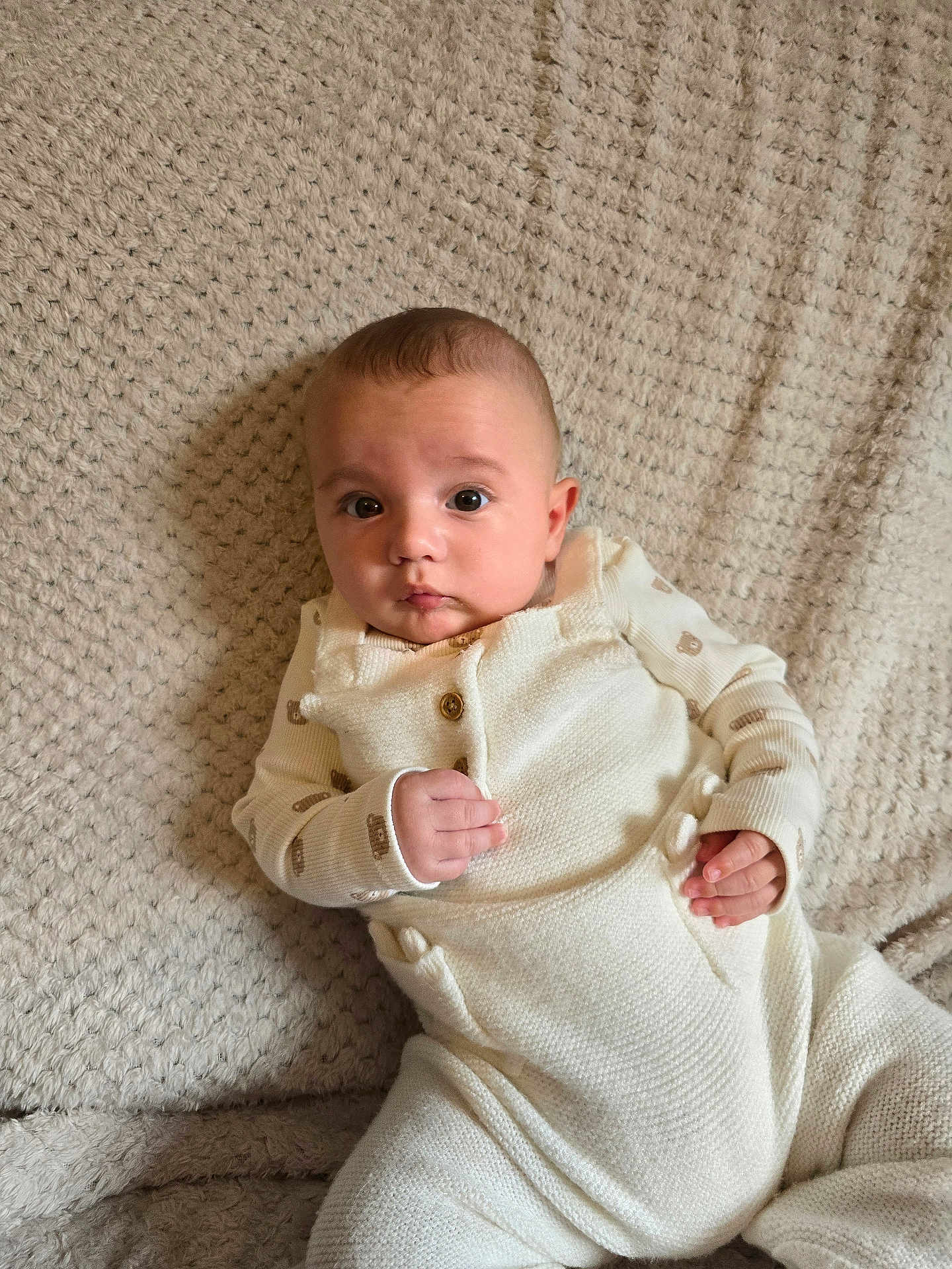 Tobias is registered to the contest to win money with this photo: baby, infant, knitwear, blanket, beige, texture, clothing, person, portrait, cute, indoor, child, small_hands, sitting, cozy, soft, warm, looking, curious, expression