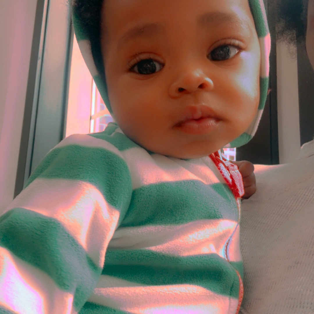 Izreal joined the competition — help win amazing prizes! baby, child, hoodie, striped_clothing, indoor, window, natural_light, close_up, portrait, curious, person, infant, cute, young_child, warm_light, soft_texture, face, expression, cozy, holding