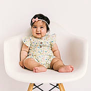Amara joined the competition — help win amazing prizes! baby, child, infant, sitting, chair, portrait, smiling, happy, headband, bow, floral_outfit, dress, bare_feet, toes, indoor, studio, white_background, furniture, photography, cute