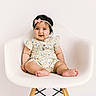 baby, child, infant, sitting, chair, portrait, smiling, happy, headband, bow, floral_outfit, dress, bare_feet, toes, indoor, studio, white_background, furniture, photography, cute