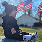 Luis joined the competition — help win amazing prizes! child, toddler, beanie, pom_pom_hat, profile, socks, bench, memorial_bench, american_flag, flags, sunflare, bokeh, shallow_depth_of_field, outdoor, grass, portrait, candid, winter_clothing, soft_light, sitting