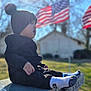 child, toddler, beanie, pom_pom_hat, profile, socks, bench, memorial_bench, american_flag, flags, sunflare, bokeh, shallow_depth_of_field, outdoor, grass, portrait, candid, winter_clothing, soft_light, sitting