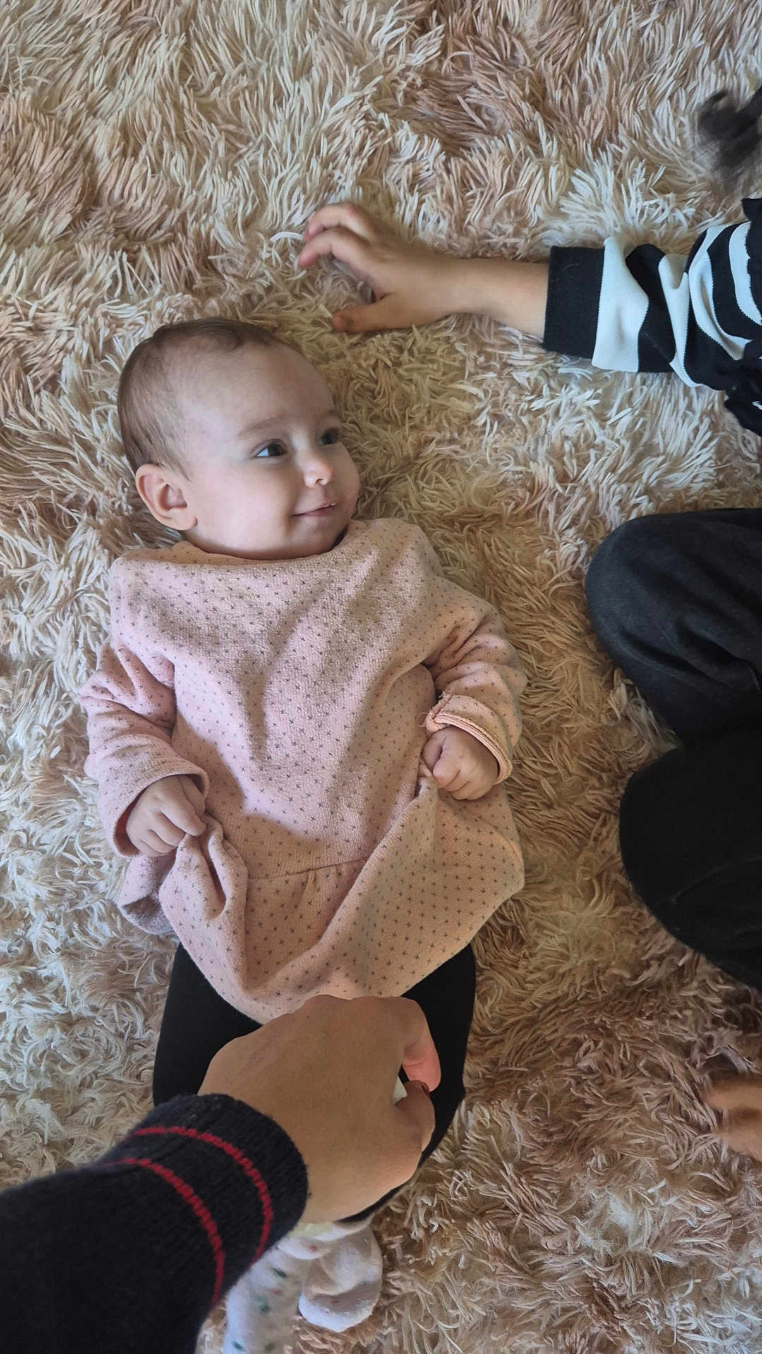 Ayla a rejoint le concours — aidez-le/la à gagner de superbes lots ! baby, child, hand, pink_clothing, rug, fluffy_rug, smile, person, infant, indoor, soft_texture, black_pants, striped_sleeve, footwear, playful, family, casual, human, cute, relaxing