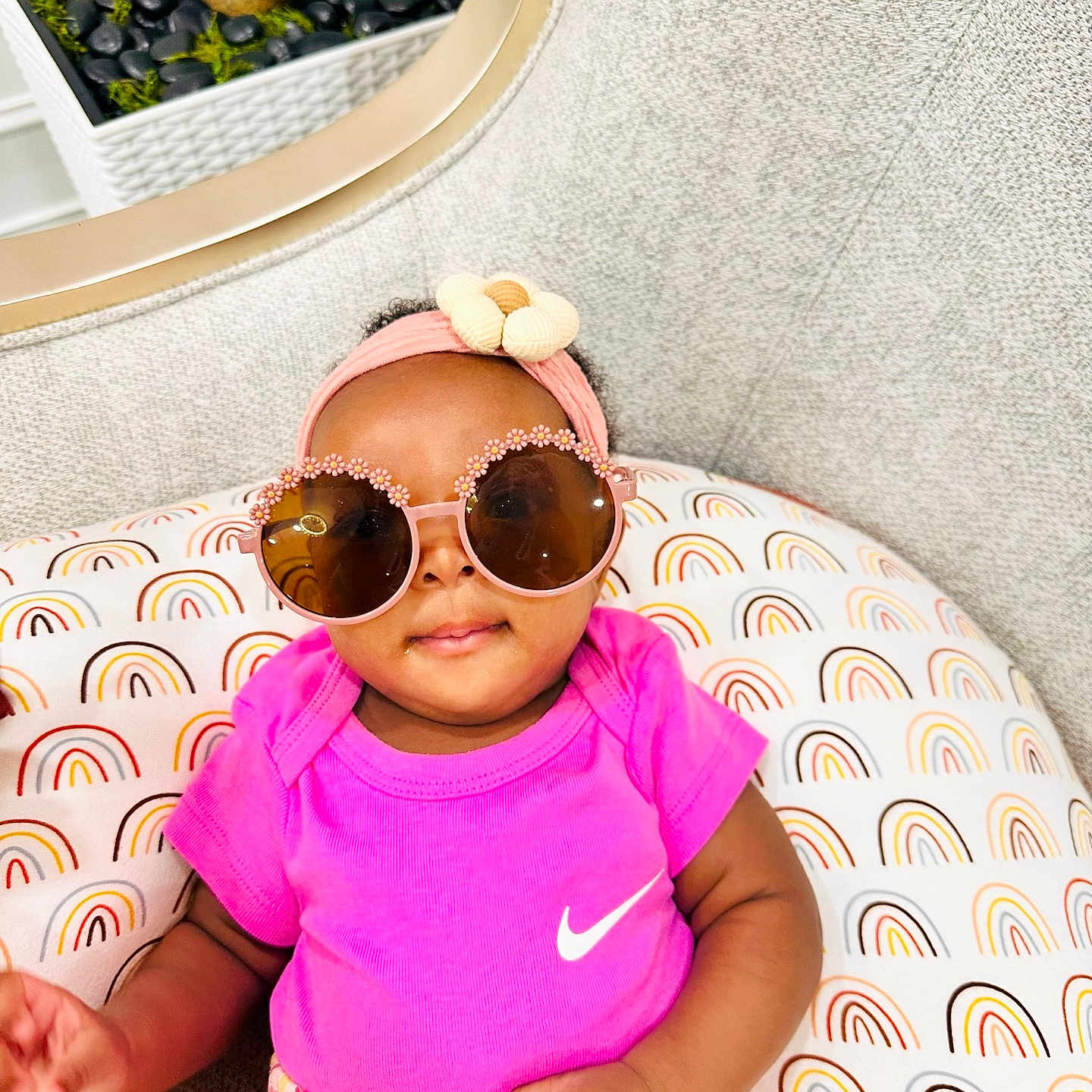 Cynthia is registered to the contest to win money with this photo: baby, child, sunglasses, headband, pink_shirt, floral_skirt, rainbow_pattern, cushion, indoor, plant, decor, fashion, cute, portrait, infant, smiling, accessory, colorful, happy, cozy