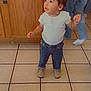 Gabby is registered to the contest to win money with this photo: toddler, child, indoor, kitchen, tile_floor, jeans, white_top, shoes, curly_hair, person, cabinet, wood, floor, standing, looking_up, casual_clothing, bracelet, earrings, curious_expression, movement