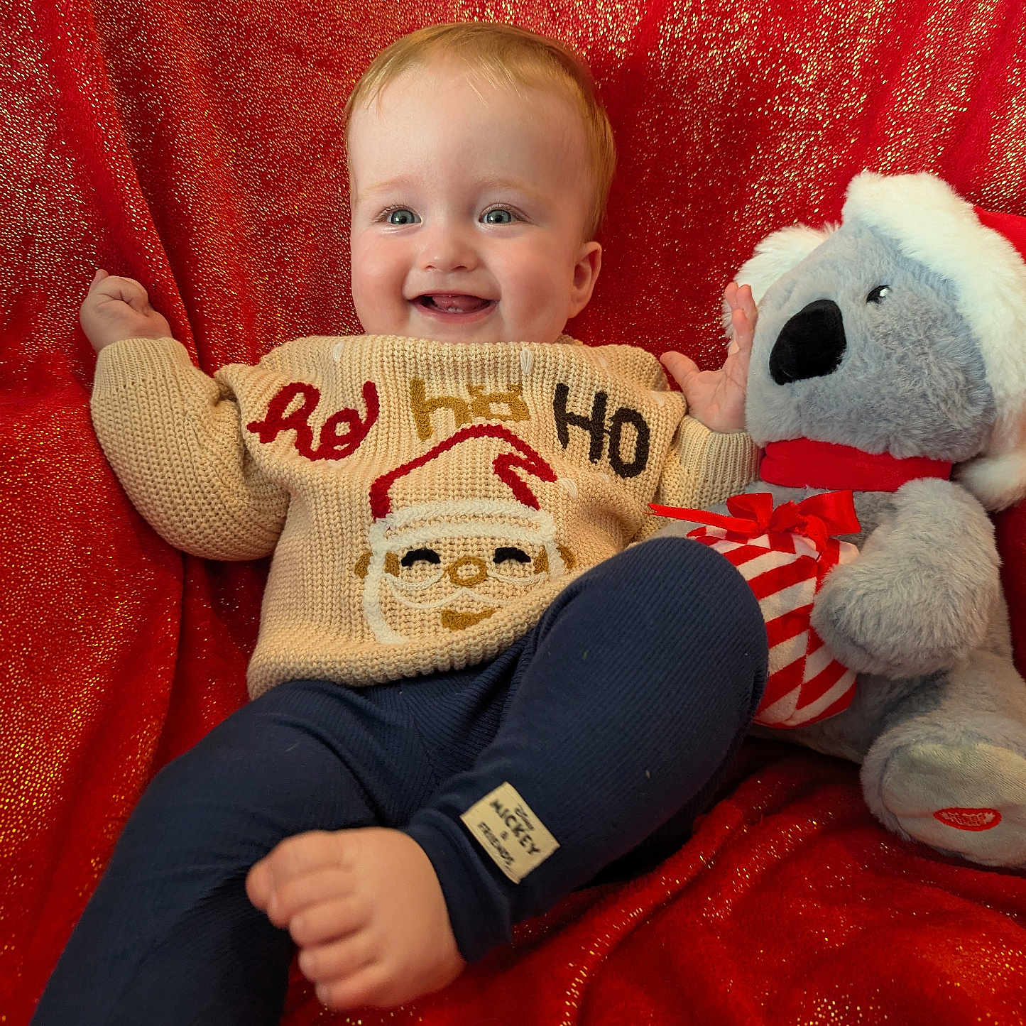 Finn is registered to the contest to win money with this photo: baby, blue_pants, cheerful, child, christmas, cuddly, cute, festive, happy, holiday, holiday_season, indoor, koala, plush_toy, portrait, red_background, santa, smiling, sweater, toy