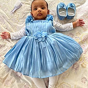 Madiha joined the competition — help win amazing prizes! baby, blue_dress, baby_shoes, baby_brush, bedspread, infant, face, arms, white_tights, floral_pattern, lying_down, cute, child, person, indoors, soft_lighting, portrait, baby_clothing, newborn, small_hands