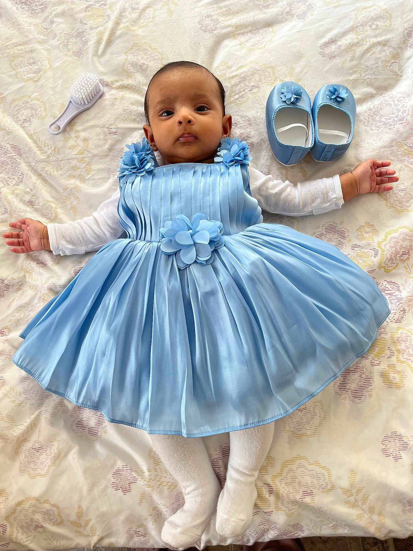 Madiha joined the competition — help win amazing prizes! baby, blue_dress, baby_shoes, baby_brush, bedspread, infant, face, arms, white_tights, floral_pattern, lying_down, cute, child, person, indoors, soft_lighting, portrait, baby_clothing, newborn, small_hands