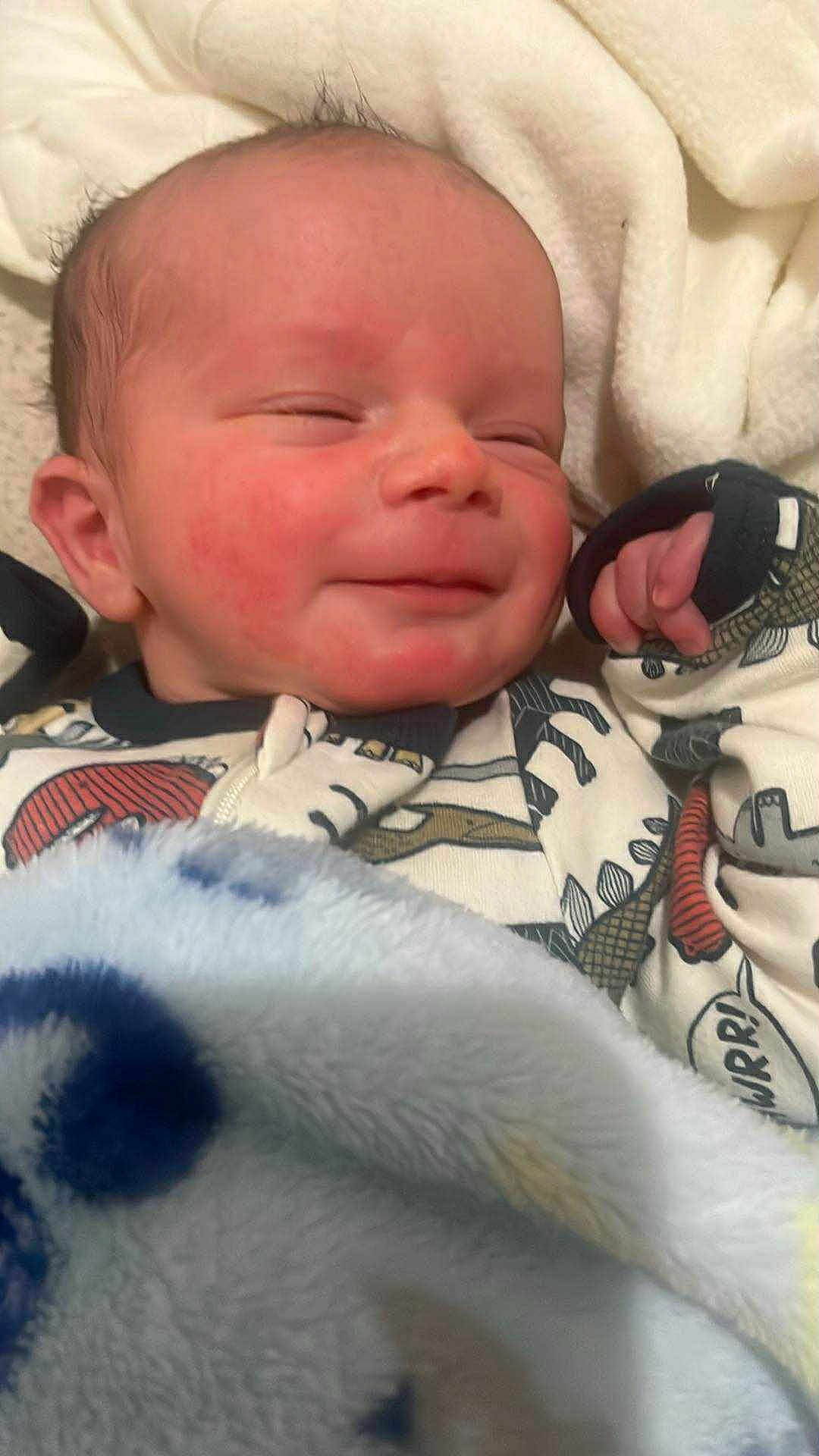 Ryker joined the competition — help win amazing prizes! newborn, baby, blanket, sleeping, smile, infant, onesie, dinosaur, cozy, cute, child, soft, warm, face, hand, portrait, indoors, resting, toddler, sleepy