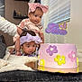 baby, birthday_cake, blanket, bow, celebration, child, curious, cute, decor, family, flower, headband, indoor, person, pink, purple, smiling, table, toddler, yellow