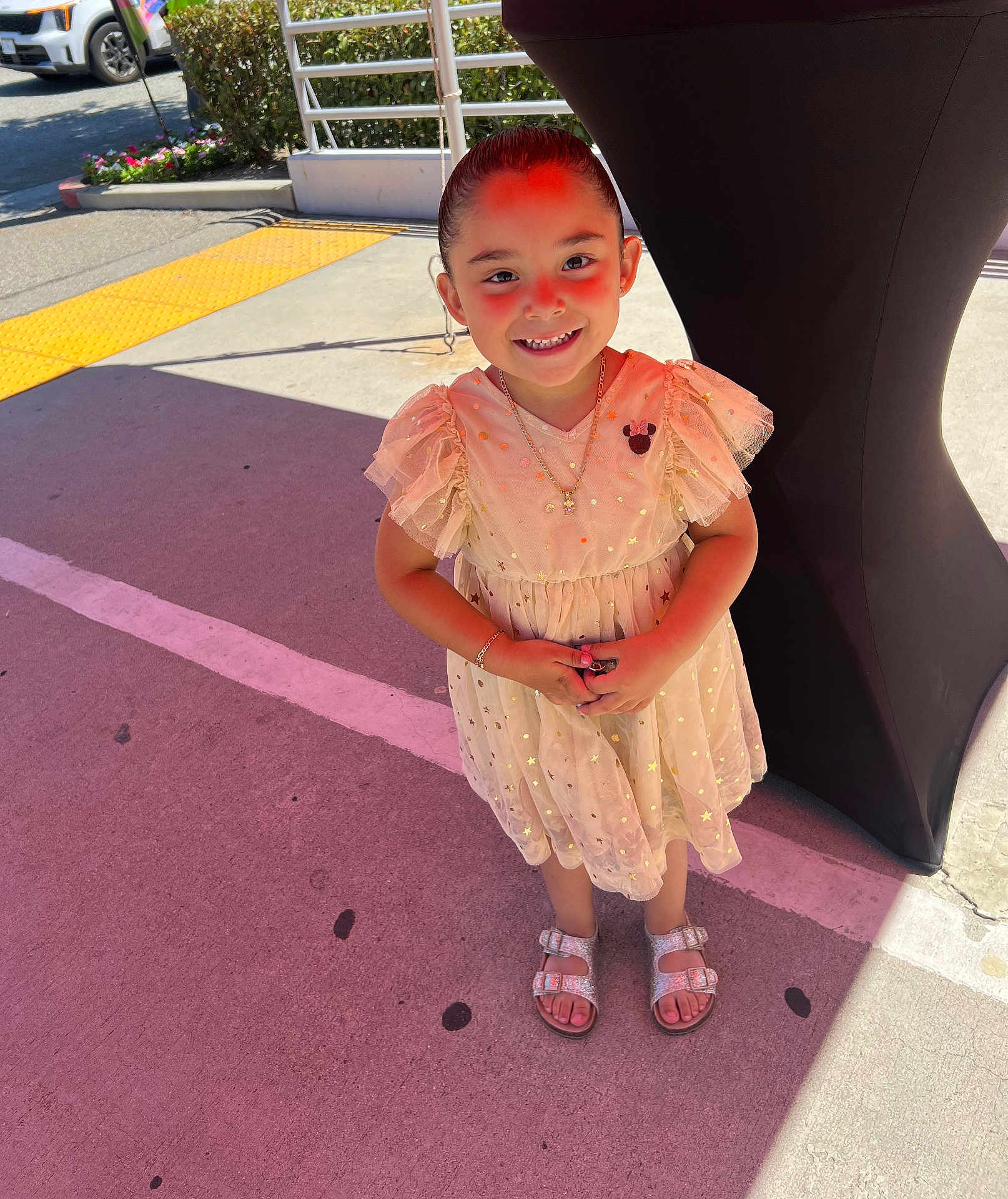 Destinie is registered to the contest to win money with this photo: child, girl, smile, dress, sparkly, sandals, outdoor, pavement, sunlight, shadow, happy, person, standing, necklace, bracelet, concrete, background, flowerbed, car, railing