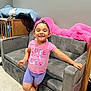 Destinie is registered to the contest to win money with this photo: child, girl, smiling, standing, pink_shirt, purple_shorts, gold_chain, gray_couch, pink_pillow, indoor, carpet, furniture, happy, casual_clothing, barefoot, room, wooden_crib, blanket, bracelet, portrait