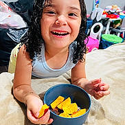 Destinie is registered to the contest to win money with this photo: child, smiling, curly_hair, wet_hair, blue_bowl, mango, food, chili_powder, blanket, indoor, toys, colorful, happy, face, hand, arm, person, playing, bedroom, casual