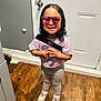 child, smiling, indoor, standing, sunglasses, pink, leggings, sneakers, wooden_floor, door, wall, light_purple_shirt, happy, fashion, cute, person, hair, bracelet, accessory, floor