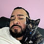 man, beard, cat, kitten, tortoiseshell_cat, collar, blue_bell, pet, indoor, pink_wall, couch, white_shirt, relaxed, portrait, closeup, feline, companion, face, human, resting