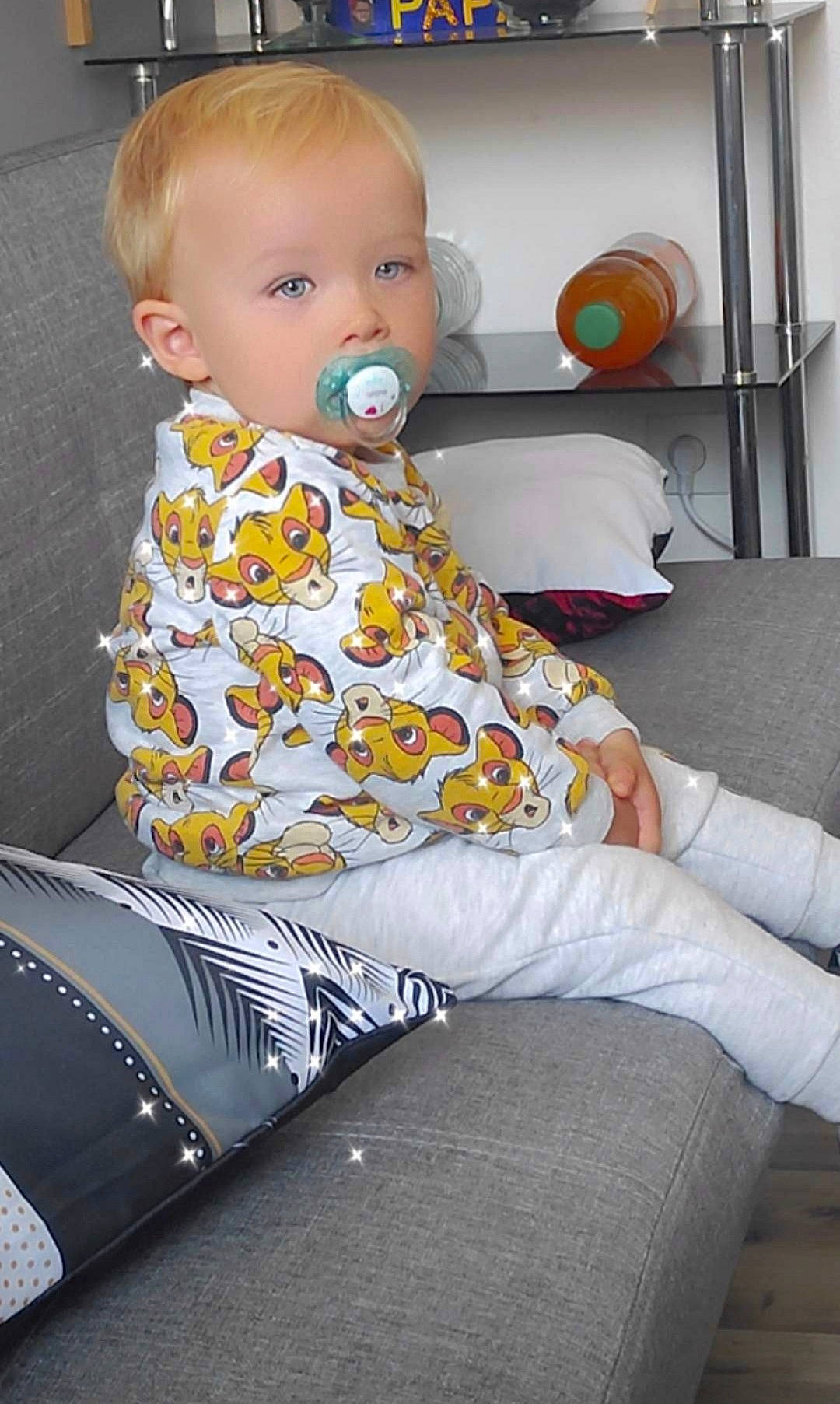 Jérôme participe au concours pour gagner de l'argent avec cette photo : baby, baby_toddler_clothing, blond, child, comfort, couch, eye, flooring, fun, hairstyle, head, human_leg, knee, lap, person, sitting, sleeve, standing, t_shirt, thigh
