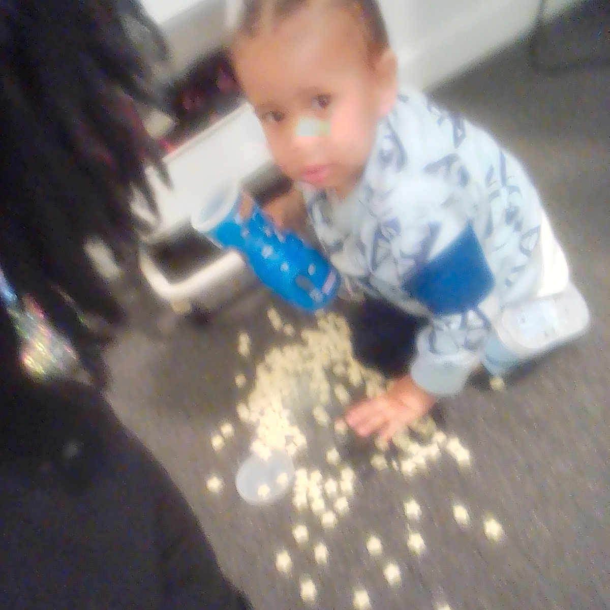 Kentrell Simmons is registered to the contest to win money with this photo: adult_partial, blue_container, blurred, carpet, casual, child, clothing, curious, face, floor, hair, hand, home, indoor, messy, person, popcorn, spill, toddler, young_child