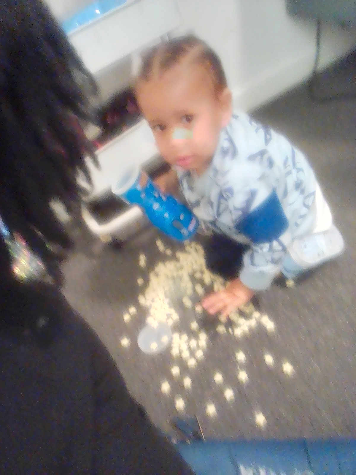 Kentrell Simmons is registered to the contest to win money with this photo: toddler, child, popcorn, spill, carpet, blue_container, indoor, messy, person, hair, clothing, floor, hand, adult_partial, curious, blurred, face, young_child, casual, home