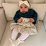 baby, child, headband, bow, sweater, skirt, floral_pattern, socks, white_socks, armchair, plush, cozy, curious, seated, indoor, portrait, cute, small_hands, textile, fashion