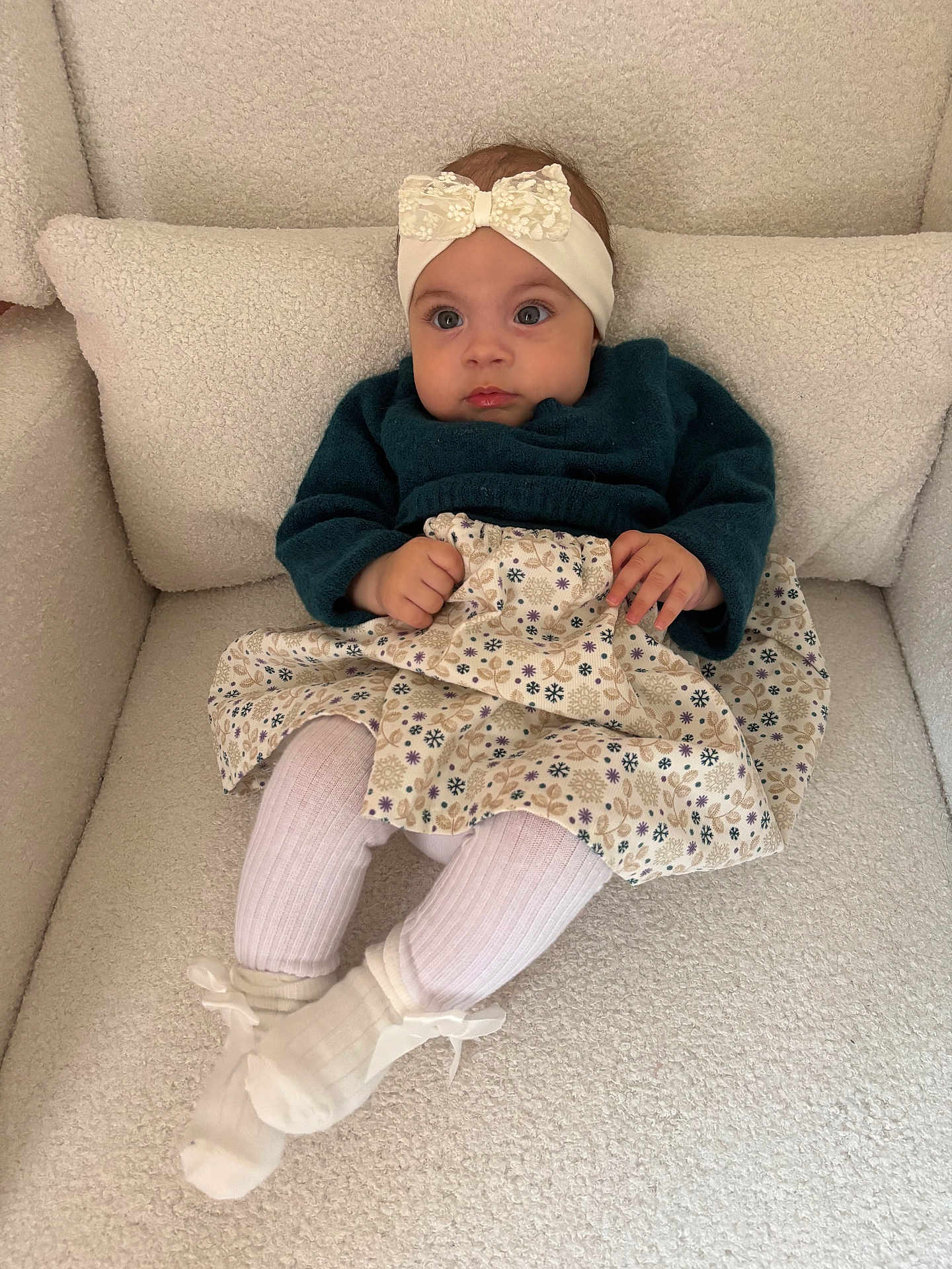 Veroccilia participe au concours pour gagner de l'argent avec cette photo : baby, child, headband, bow, sweater, skirt, floral_pattern, socks, white_socks, armchair, plush, cozy, curious, seated, indoor, portrait, cute, small_hands, textile, fashion