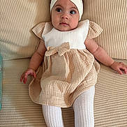 Veroccilia participe au concours pour gagner de l'argent avec cette photo : baby, child, infant, dress, headband, bow, couch, beige, white, tights, sitting, cute, portrait, indoors, soft_texture, clothing, relaxed, young, person, furniture