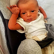 Axel is registered to the contest to win money with this photo: baby, newborn, infant, child, white_onesie, blanket, cushion, seat, indoor, face, arm, hand, skin, expression, resting, portrait, clothing, comfort, young, person