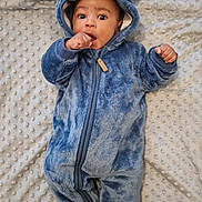 Milo is registered to the contest to win money with this photo: baby, infant, blue_onesie, hooded_clothing, bear_ears, blanket, textured_blanket, lying_down, cute, wide_eyes, hand_near_mouth, fuzzy_clothing, warm, cozy, indoors, child, portrait, soft_texture, adorable, expression