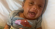 Arimani is registered to the contest to win money with this photo: baby, infant, child, smiling, tongue_out, portrait, lying_down, bed, pillow, blanket, striped_shirt, dinosaur_print, indoors, happy, playful, face, hands, bedding, close_up, photography