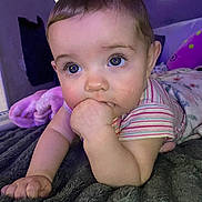 Leilani is registered to the contest to win money with this photo: baby, child, infant, portrait, face, eyes, curious, sitting, lying_down, hand, fist, chewing, striped_shirt, clothing, blanket, bedroom, pillow, soft_lighting, indoor, closeup