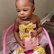 Majesty is registered to the contest to win money with this photo: baby, child, girl, pink_chair, pink_bow, gold_bow, tutu, pink_purse, white_socks, yellow_ruffles, jewelry, earrings, necklace, arm_band, sitting, indoor, flooring, cute, fashion, portrait