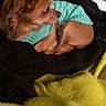 dog, small_dog, brown_dog, fluffy, long_hair, sweater, turquoise, curled_up, sleeping_area, blanket, black_blanket, yellow_blanket, cozy, indoors, pet, animal, side_view, resting, home, cute