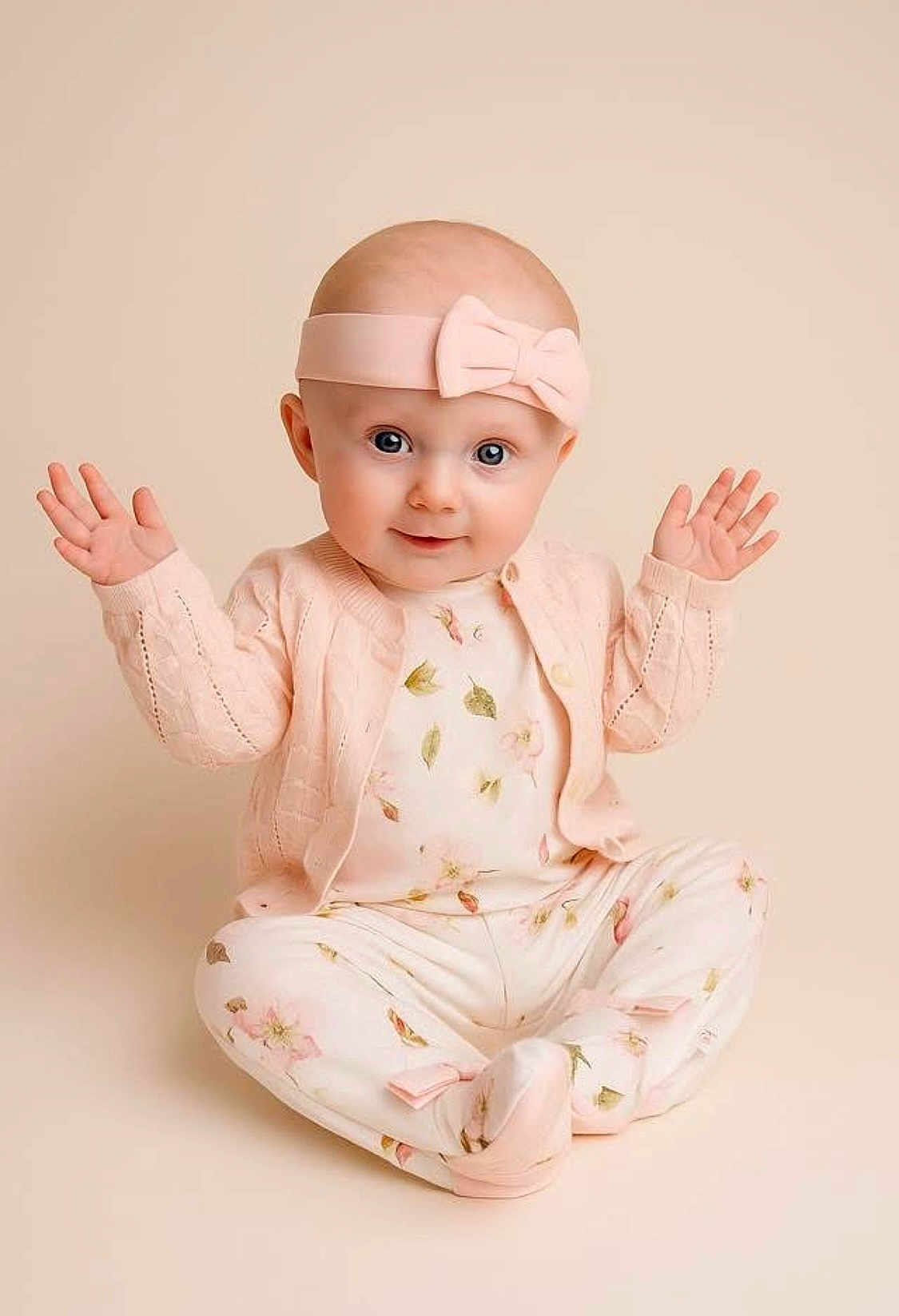 Leonie is registered to the contest to win money with this photo: baby, infant, child, pink_headband, bow, floral_pajamas, cardigan, sitting, raised_hands, cute, portrait, studio, soft_lighting, smiling, innocent, pastel_colors, face, eyes, hands, background