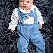 Micahel Jr is registered to the contest to win money with this photo: baby, infant, blue_clothing, bow_tie, suspenders, white_shirt, fluffy_rug, portrait, cute, child, newborn, fashion, soft_texture, lying_down, indoor, small_feet, face, expression, hands, foot