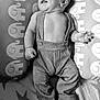 baby, infant, smiling, suspenders, pants, cushion, elephant_pattern, lying_down, happy, cute, child, portrait, black_and_white, soft_lighting, indoors, cozy, small_hands, feet, expression, relaxed