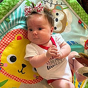 Daphne is registered to the contest to win money with this photo: baby, bow, child, chubby_cheeks, clothing, colorful, cute, expression, face, hands, indoor, infant, lion, monkey, patterned, playmat, red_trim, soft_toy, toy, white_onesie