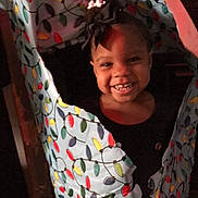 Erica is registered to the contest to win money with this photo: child, toddler, smile, face, hair_bow, clothing, pattern, colorful, light_bulbs, fabric, torn, happy, indoor, portrait, person, cute, dark_background, cheerful, playful, young