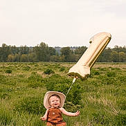 Royal is registered to the contest to win money with this photo: toddler, child, balloon, number_one, cowboy_hat, overalls, grass, field, outdoor, nature, happy, smiling, celebration, greenery, baby, one_year_old, sunny, playful, portrait, casual