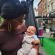 Kameron participe au concours pour gagner de l'argent avec cette photo : baby, woman, smiling, outdoor, cafe, urban, headwrap, glasses, happy, child, holding, clothing, street, table, chair, greenery, people, daylight, portrait, casual