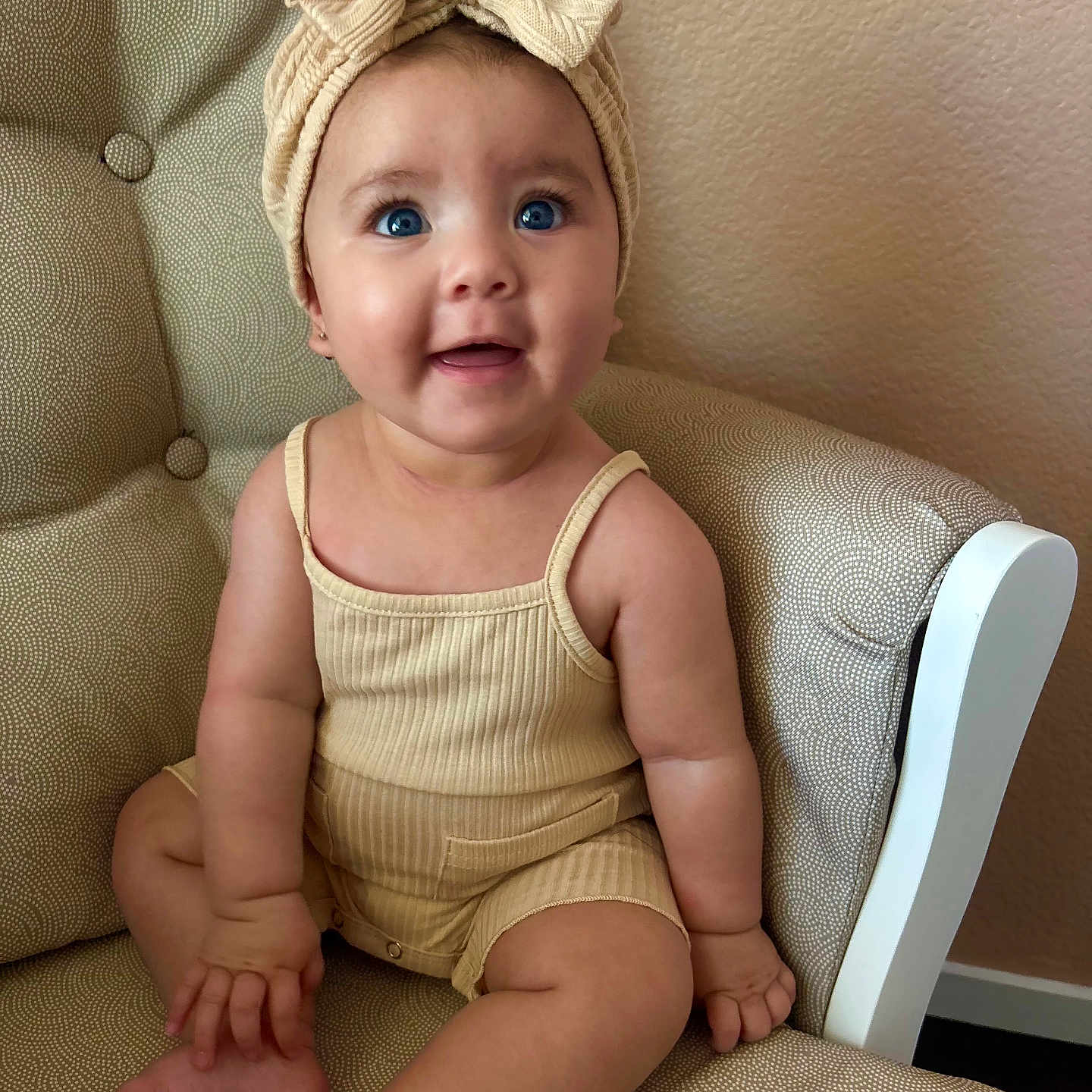 Loviena is registered to the contest to win money with this photo: armchair, baby, beige_clothing, blue_eyes, bow, child, chubby_cheeks, cute, happy, headband, indoors, infant, legs, patterned_fabric, person, portrait, sitting, skin, small_fingers, smiling