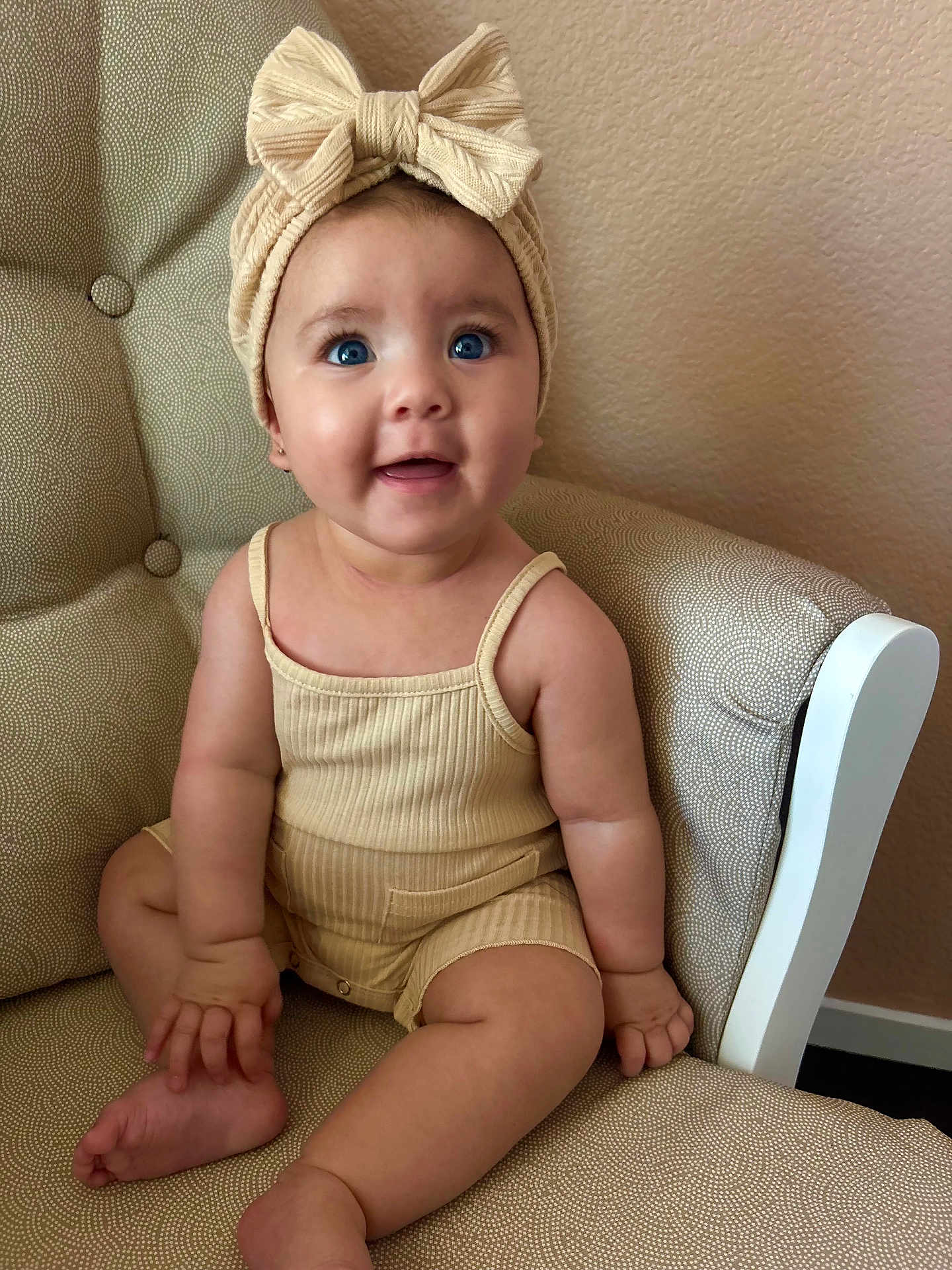 Loviena is registered to the contest to win money with this photo: baby, child, blue_eyes, headband, bow, beige_clothing, armchair, patterned_fabric, happy, smiling, sitting, infant, cute, indoors, skin, person, portrait, chubby_cheeks, small_fingers, legs
