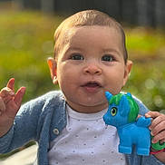 Laura a rejoint le concours — aidez-le/la à gagner de superbes lots ! baby, child, toy, unicorn, blue_cardigan, white_shirt, outdoor, portrait, cute, smiling, hand, face, young_child, nature, daylight, person, happy, clothing, infant, playful