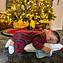 toddler, sleeping, pajamas, plaid, milk_bottle, pillow, christmas_tree, holiday, cozy, carpet, indoors, child, cute, nap, soft_lighting, decorations, festive, relaxing, home, warm
