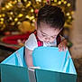 Riley is registered to the contest to win money with this photo: toddler, child, gift_box, christmas_tree, holiday, curious, indoors, soft_light, festive, present, ribbon, young_child, celebration, holiday_decorations, face, person, candid, christmas_lights, cute, exploration
